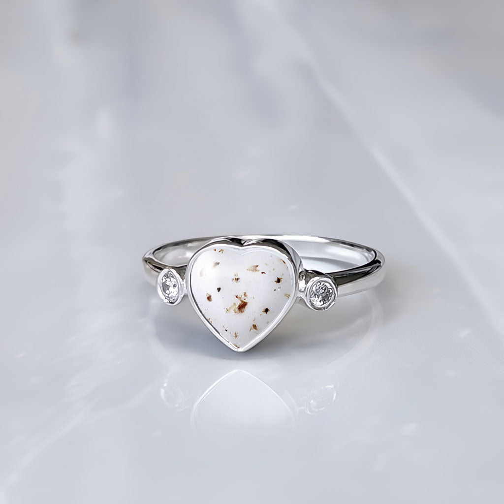 Anillo de plata con partículas de cordón umbilical dentro de un corazón con una circonita a cada lado.