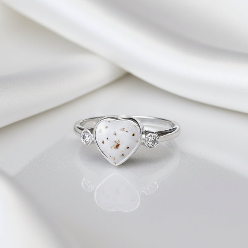 Anillo de plata con partículas de cordón umbilical dentro de un corazón con una circonita a cada lado.