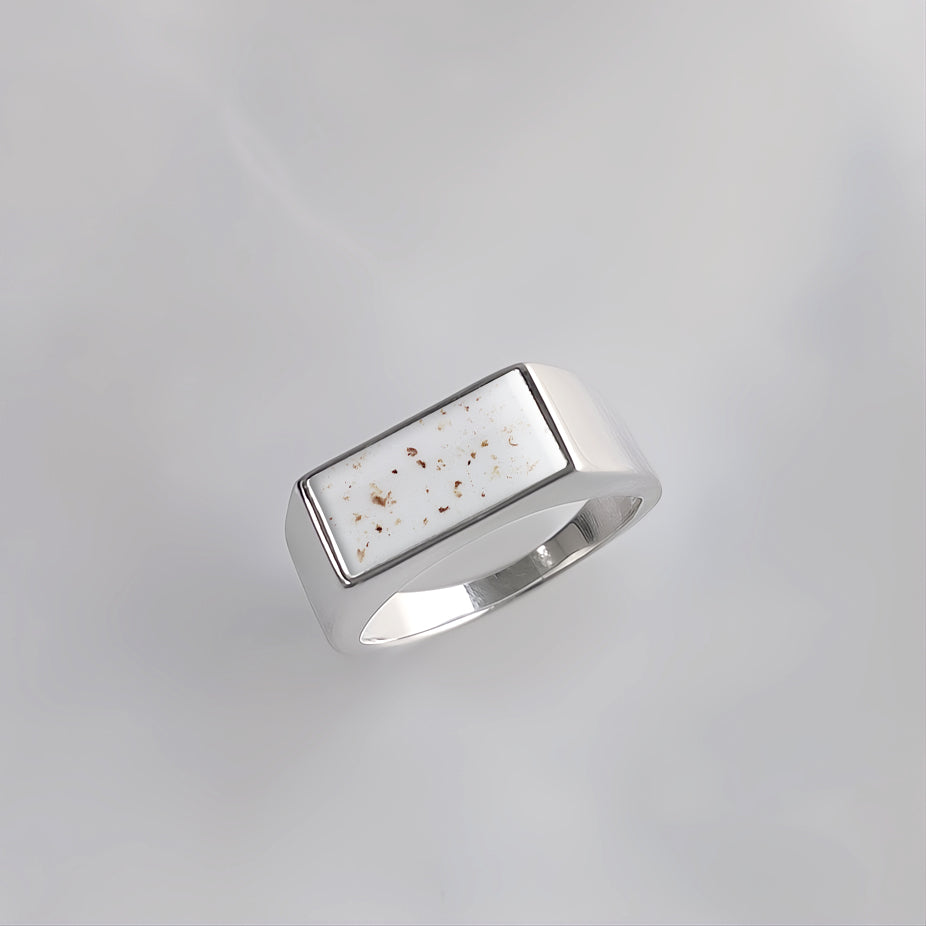 Anillo de plata con forma de sello rectangular que contiene partículas de cordón umbilical en su gema central.