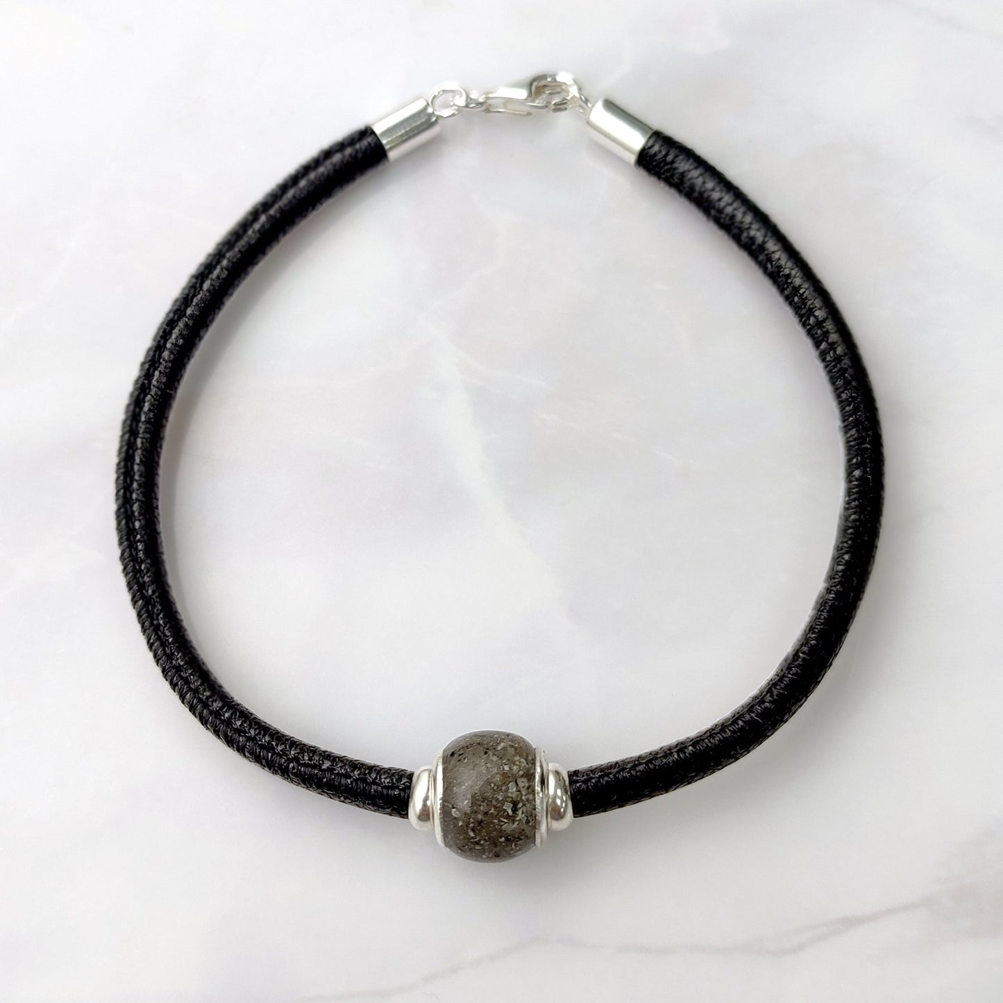 Charm con cenizas y ojales de plata dentro de pulsera de cuero