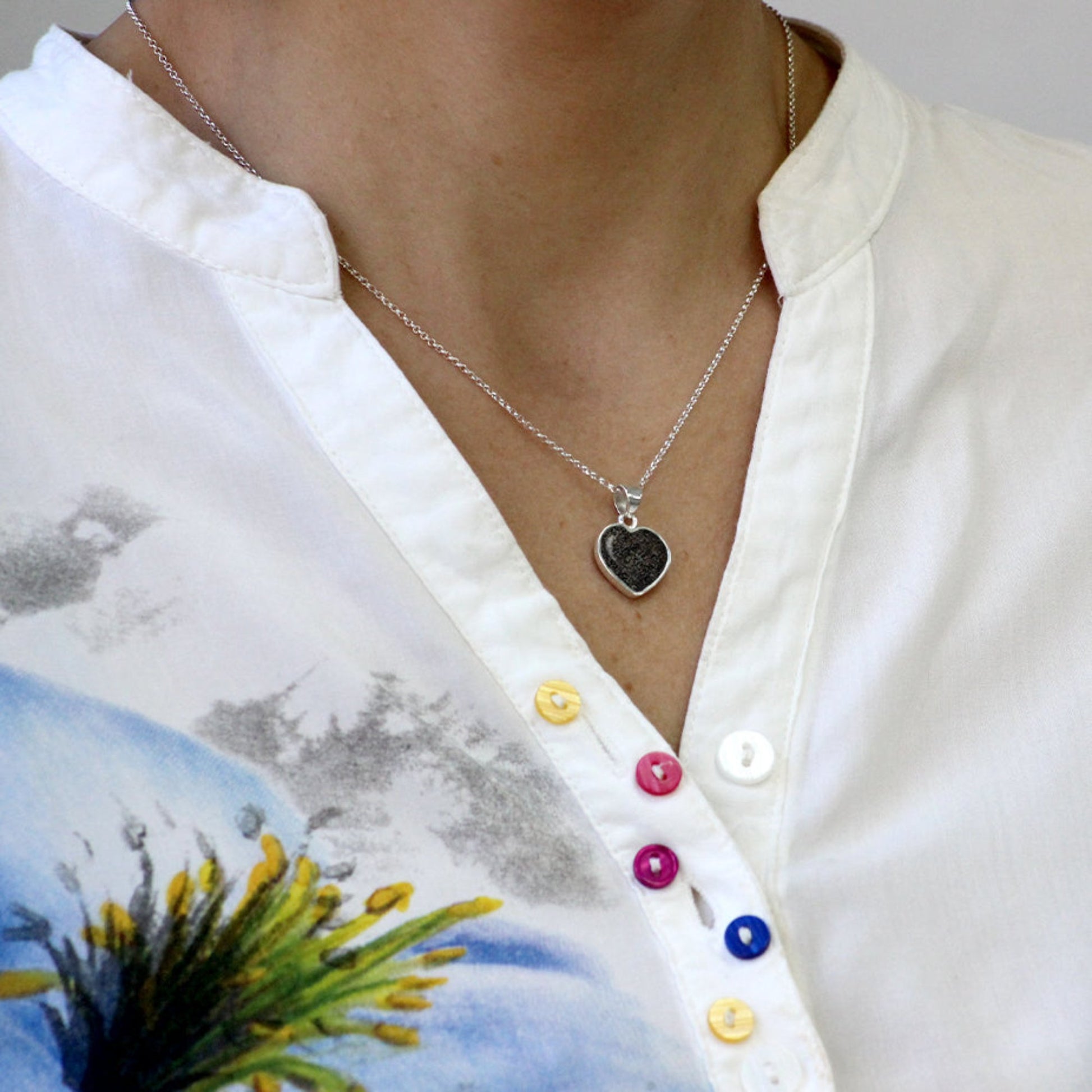 Colgante de plata con arena negra de playa en forma de corazón simple.