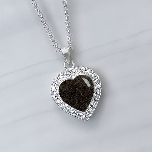 Colgante con pelo de mascota dentro de corazón de plata con circonitas alrededor.