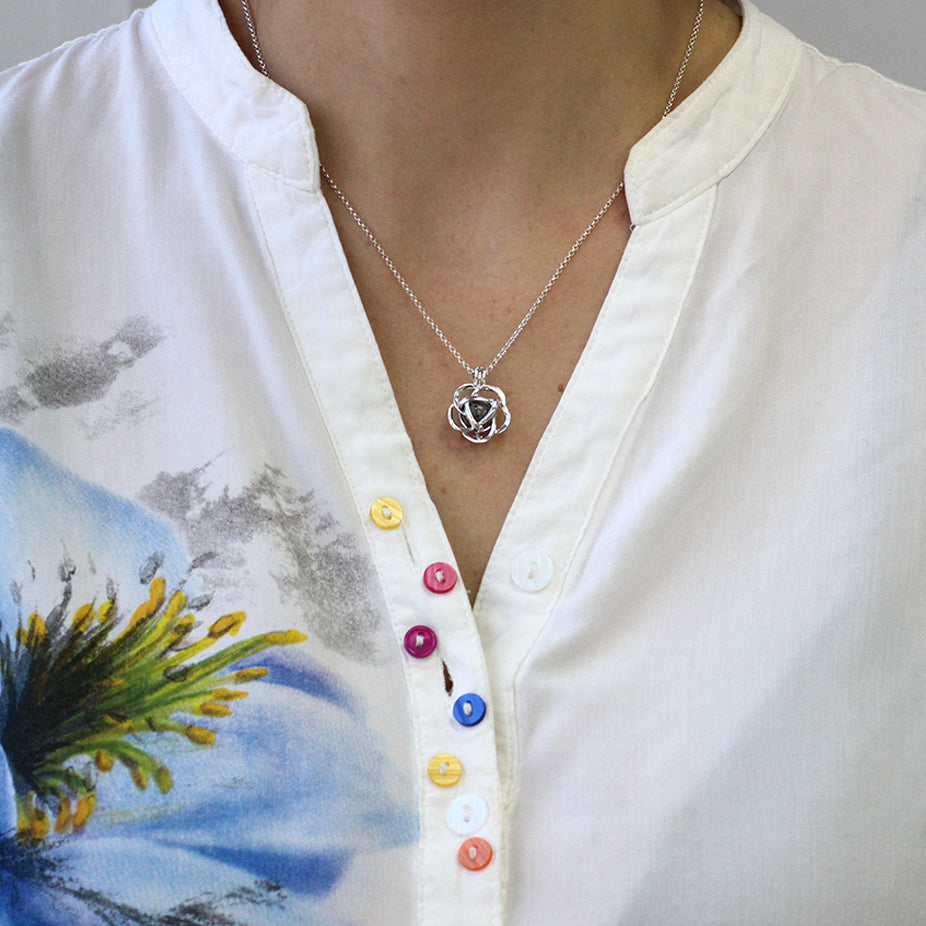 Colgante de plata con bolita de cenizas dentro de jaula en forma de flor.