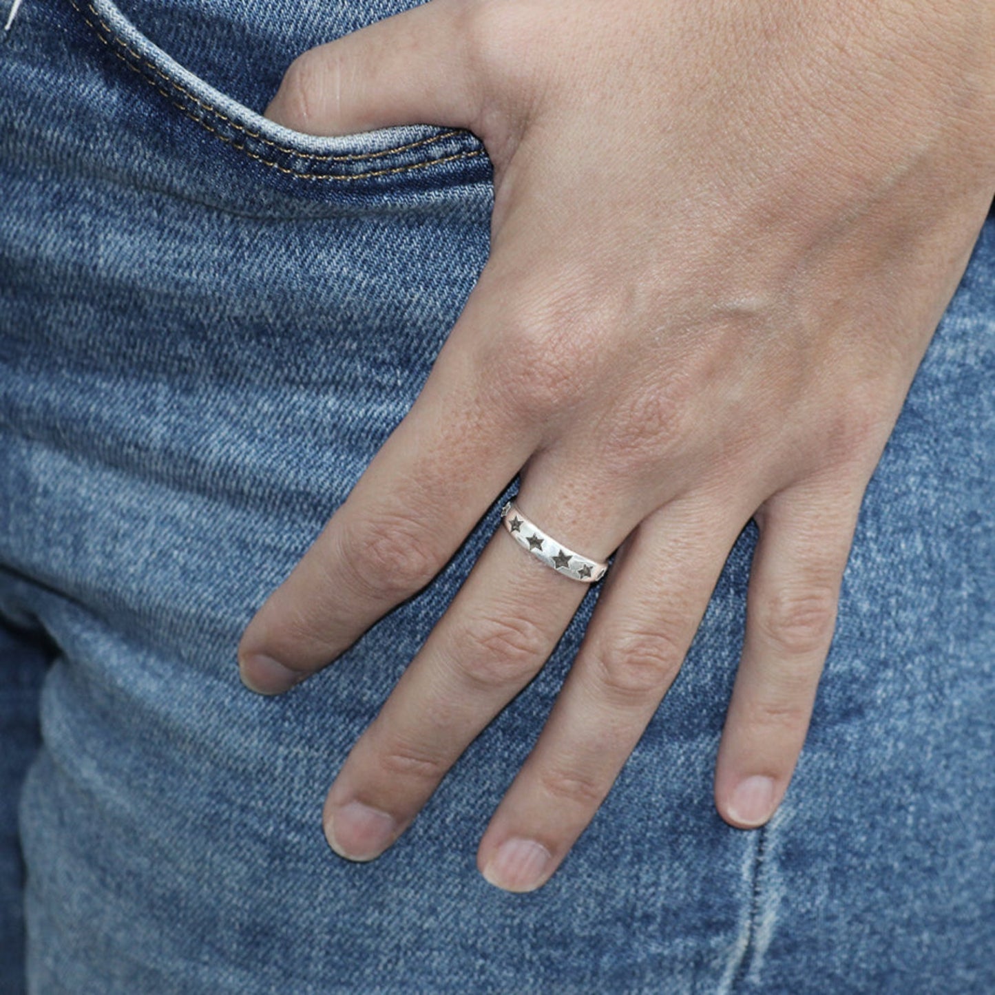 Anillo de plata con cenizas dentro de estrellas. Mano en vaquero.