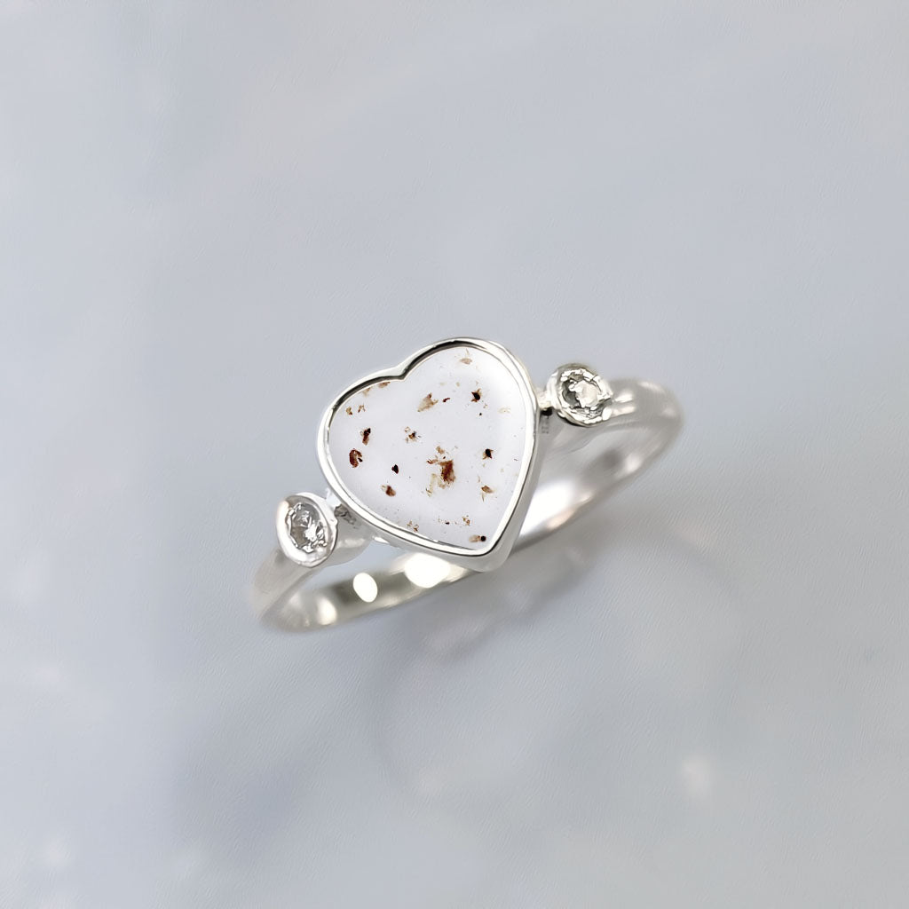 Anillo de plata con partículas de cordón umbilical dentro de un corazón con una circonita a cada lado.