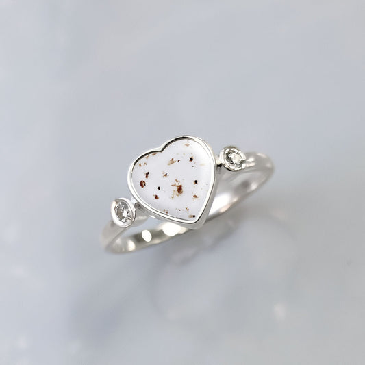 Anillo de plata con partículas de cordón umbilical dentro de un corazón con una circonita a cada lado.