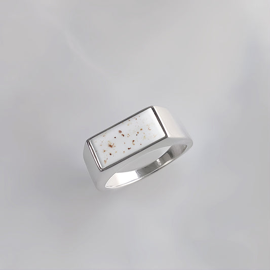 Anillo de plata con forma de sello rectangular que contiene partículas de cordón umbilical en su gema central.