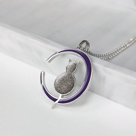 Colgante con cenizas de gato dentro de su silueta sentada sobre la luna creciente coloreada de azul.