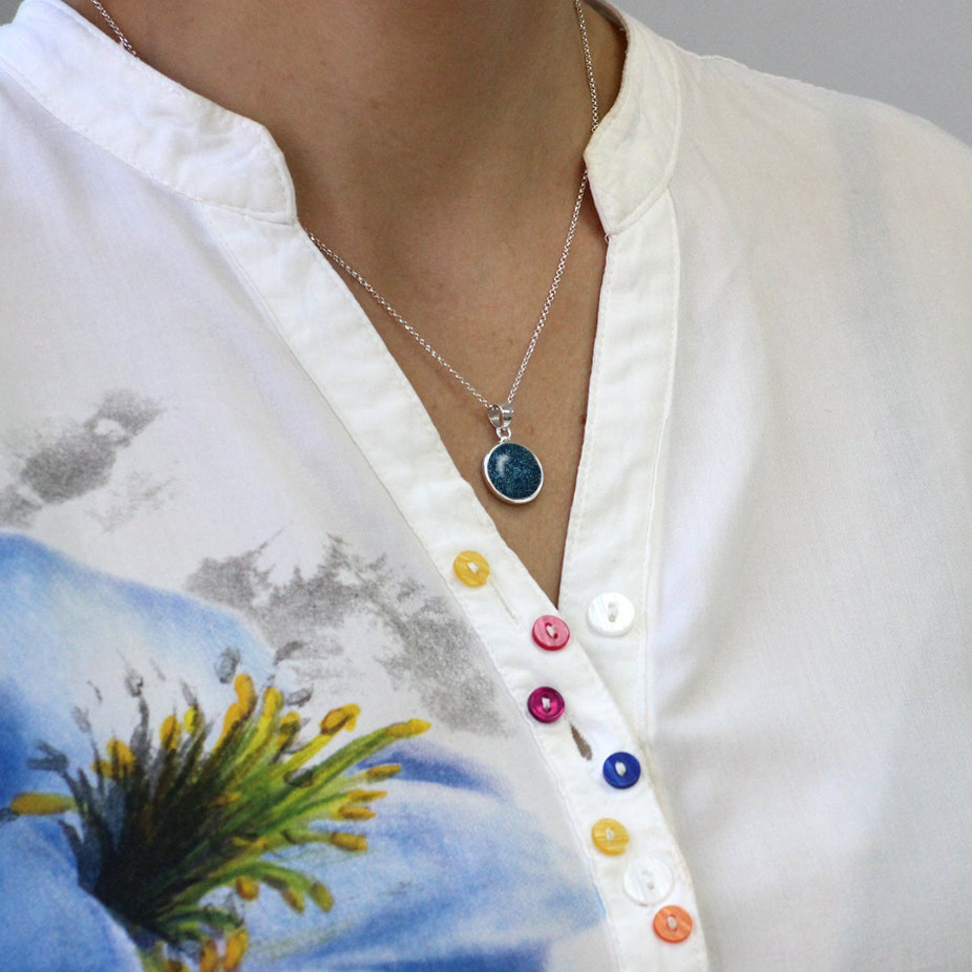 Colgante de plata con cenizas en azul en círculo.